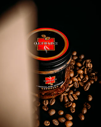 A jar of chocolate spread with an espresso flavor is placed on a black surface, surrounded by scattered coffee beans. The lid of the jar prominently displays a logo with the words 'Espoleto'. A soft light casts a shadow on the left side, creating a dramatic effect.