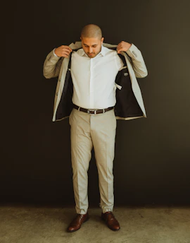 Close-up of a stylish man adjusting his tailored navy blazer against a minimalistic dark background.