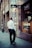 A man in formal attire is walking along a city street, passing by storefronts with prominent signage including Omega and Cartel. The scene suggests a business district atmosphere with modern architectural elements.