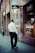 A man in formal attire is walking along a city street, passing by storefronts with prominent signage including Omega and Cartel. The scene suggests a business district atmosphere with modern architectural elements.