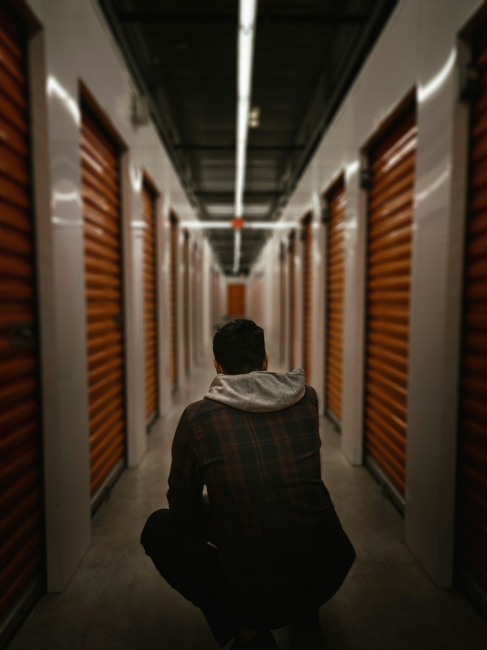 a man sitting in a hallway between two rows of storage units