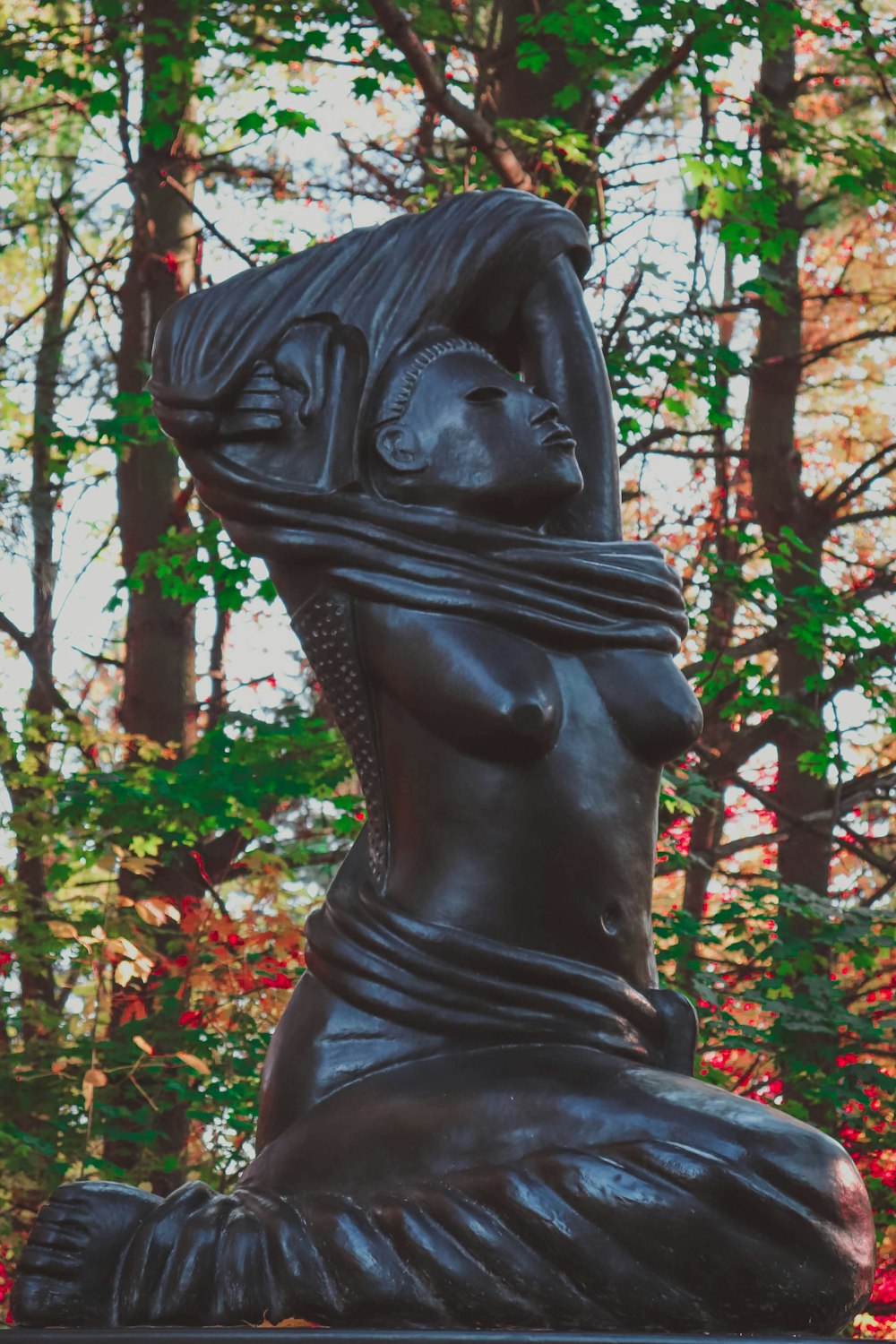 a statue of a woman sitting in the middle of a forest