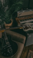 A cozy corner filled with music equipment, including an electric guitar resting on a brown sofa, an amplifier with the Fender logo, a vintage keyboard, and a woven basket containing a lush green plant. There's a sense of a creative, relaxed atmosphere.