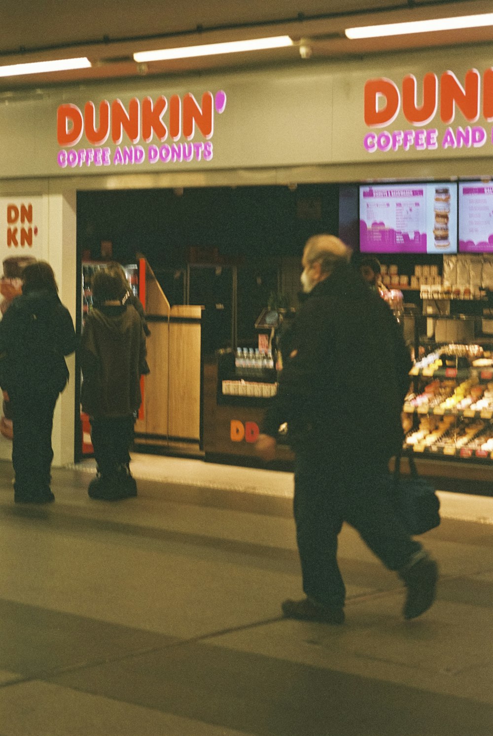 a group of people walking past a dunkin donuts store
