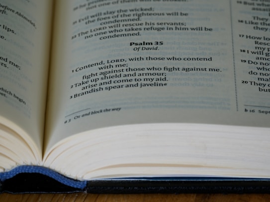 An open book displaying text from Psalm 35 on a wooden surface. The book is likely a Bible, featuring bold and regular text, with a focus on verses 1 to 3.