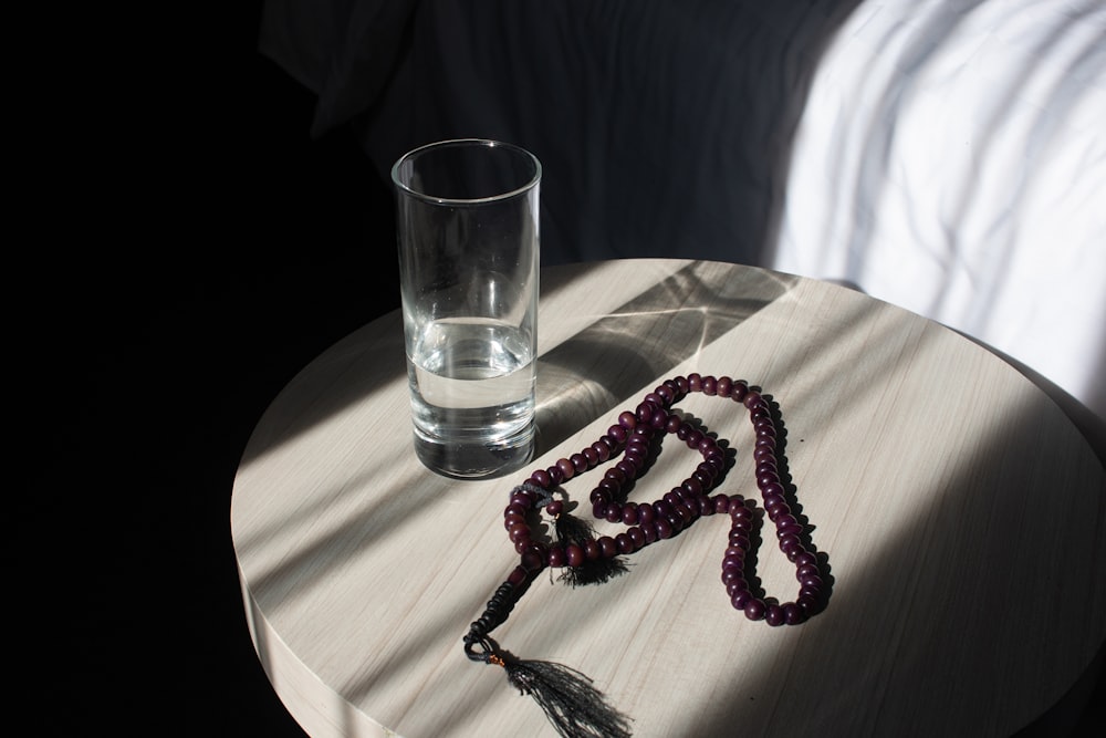 a beaded necklace sitting on a table next to a glass of water