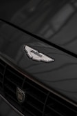 A close-up of a car's front grille displaying a prominent emblem with intricate details. The surface reflects light subtly, enhancing the elegance of the design.