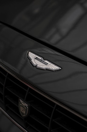 A close-up of a car's front grille displaying a prominent emblem with intricate details. The surface reflects light subtly, enhancing the elegance of the design.