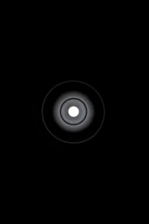 A circular, concentric pattern centered around a bright white dot, radiating darker circular gradients outward to a black background.