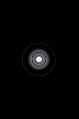 A circular, concentric pattern centered around a bright white dot, radiating darker circular gradients outward to a black background.