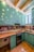 A kitchen with teal cabinets and wooden countertops. The backsplash features artistic sepia-toned images. The room has a modern stove and a stainless steel sink under a window. Exposed wooden beams are visible on the ceiling, with recessed lighting.