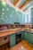 A kitchen with teal cabinets and wooden countertops. The backsplash features artistic sepia-toned images. The room has a modern stove and a stainless steel sink under a window. Exposed wooden beams are visible on the ceiling, with recessed lighting.