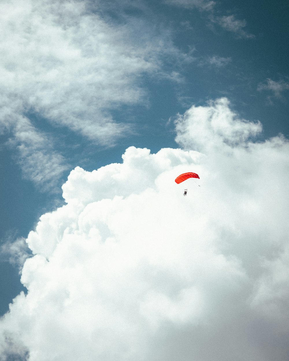 a red kite flying through a cloudy blue sky