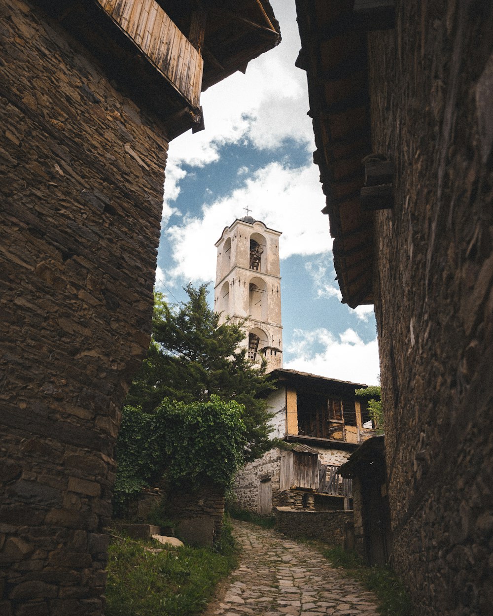 a narrow cobblestone street with a church tower in the background