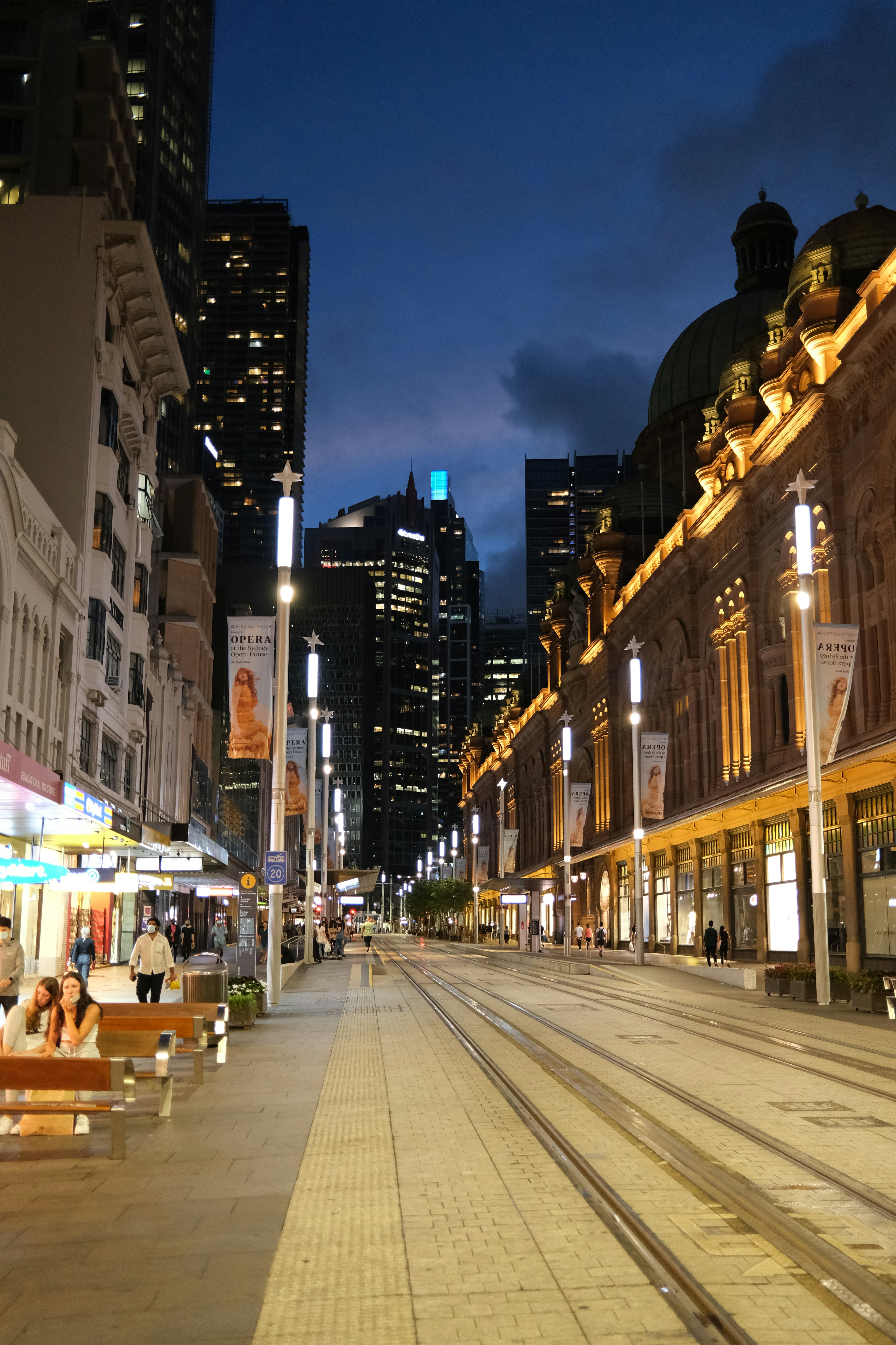 a city street at night with people sitting on benches