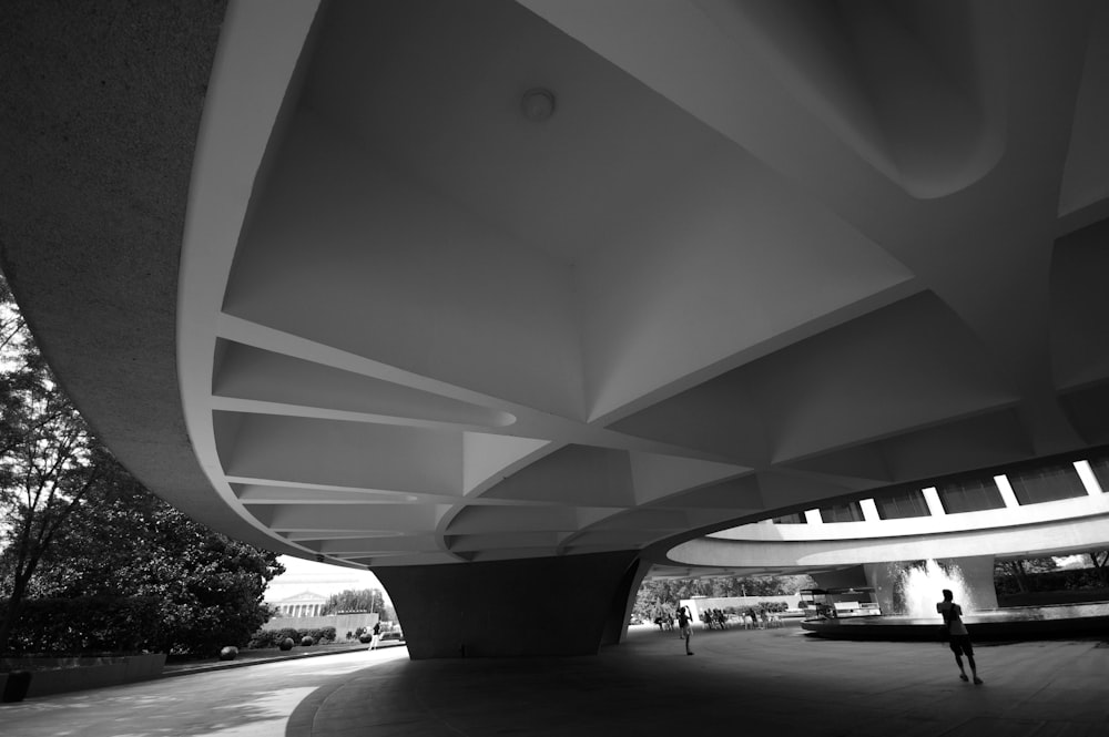 a black and white photo of a person walking under a bridge