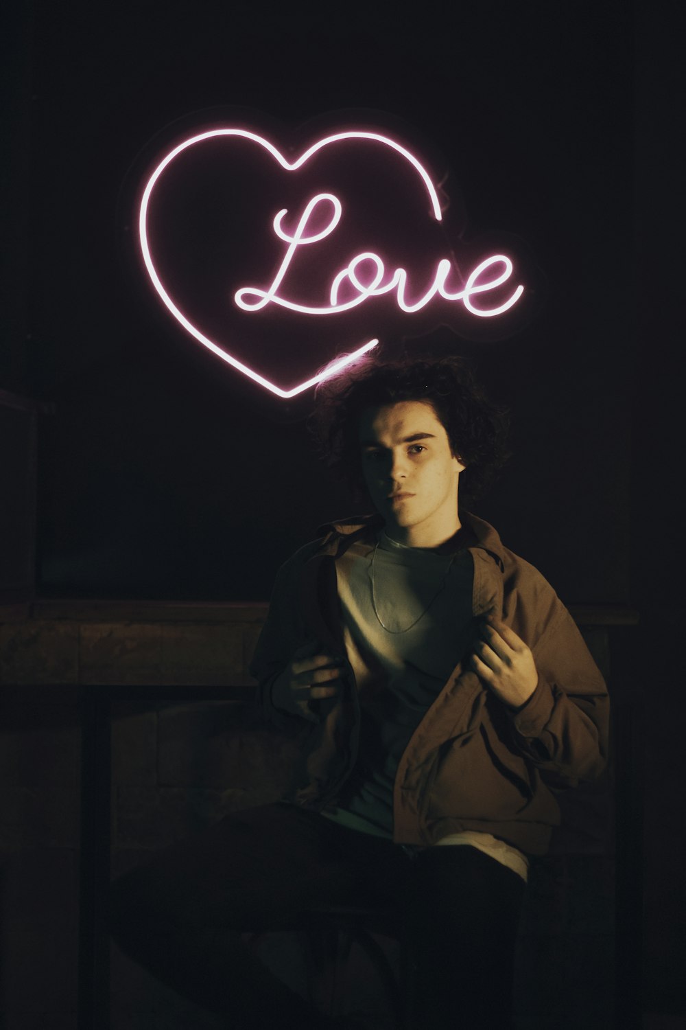 a woman sitting on a bench in front of a neon heart