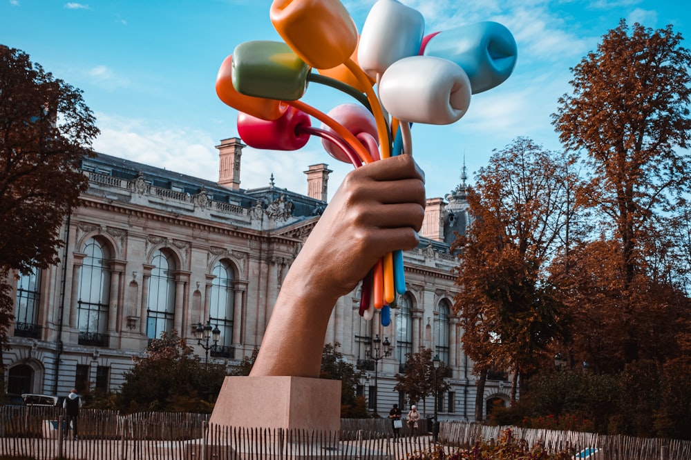 a hand holding a bunch of balloons in front of a building