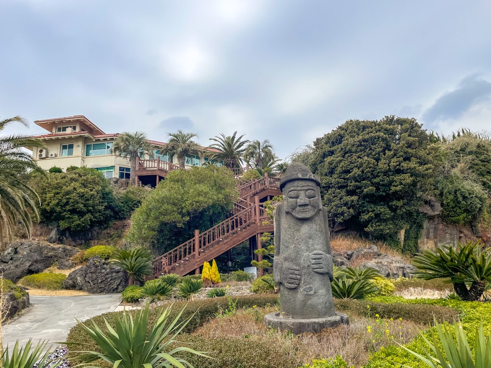 a statue in the middle of a garden with a house in the background