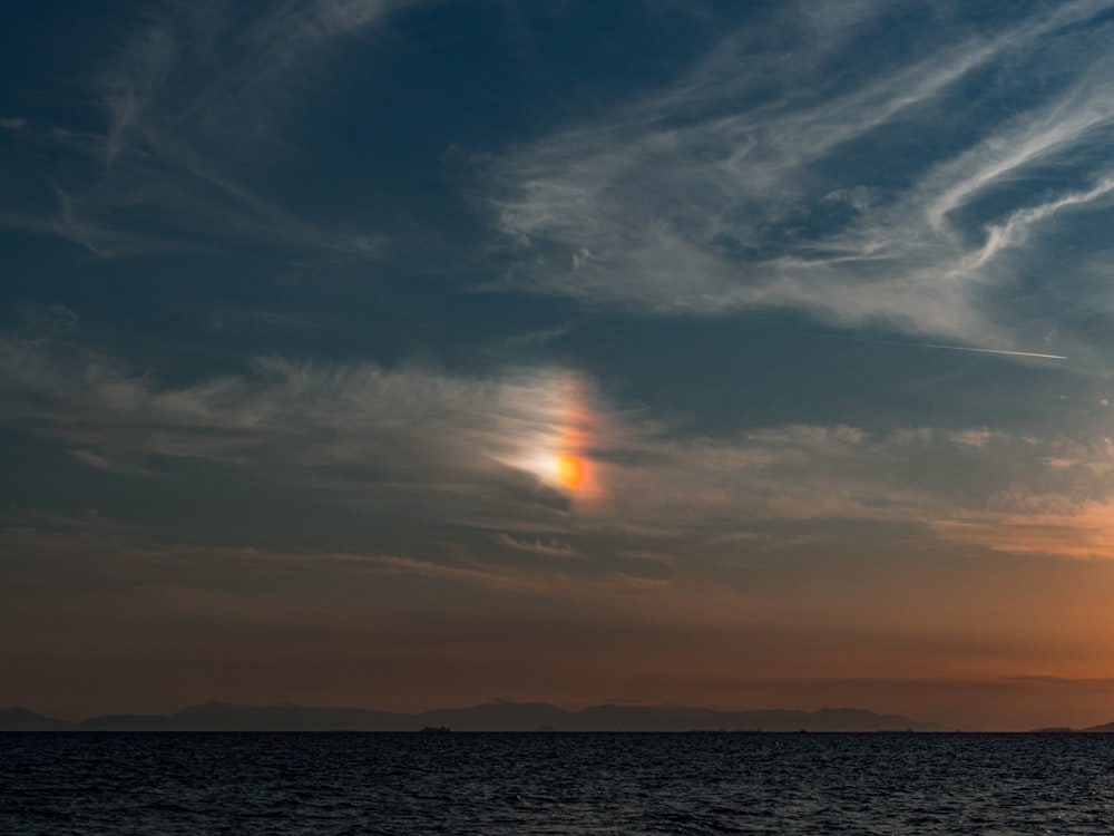 the sun is setting over the ocean with clouds in the sky