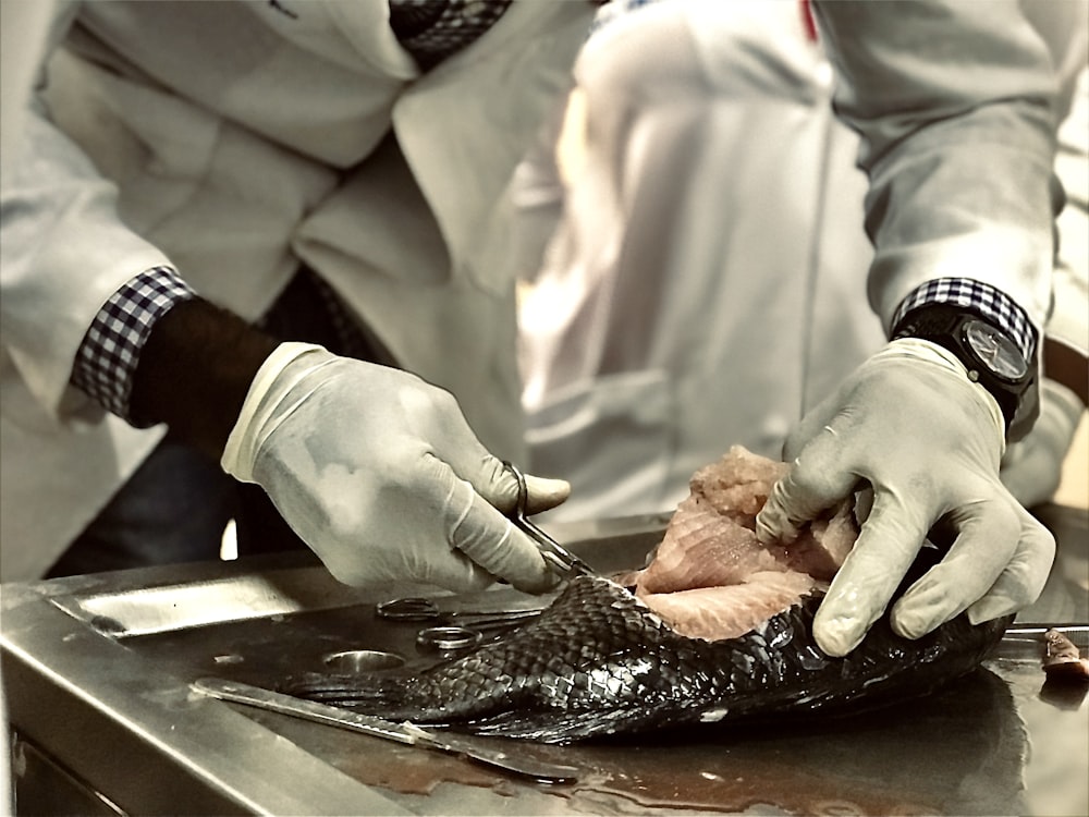 eine Person in weißen Handschuhen, die ein Stück Fisch schneidet