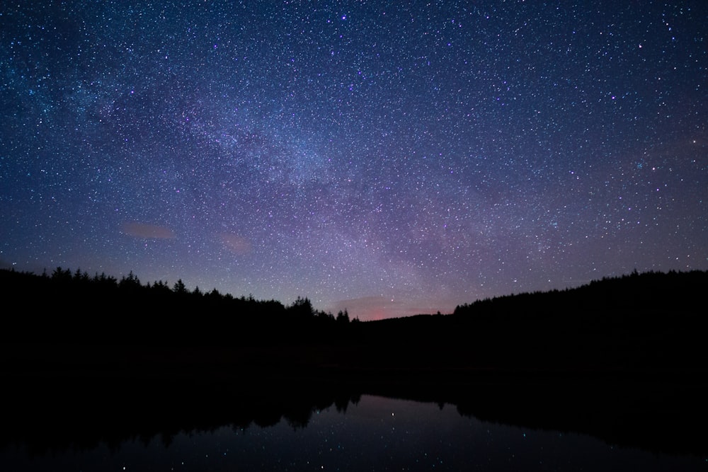 the night sky is filled with stars above a lake