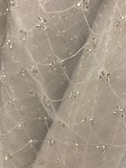 A close-up view of delicate white mesh fabric adorned with small, shiny, silver beads arranged in a subtle pattern. The fabric appears soft and lightweight, creating a sense of elegance and intricacy.