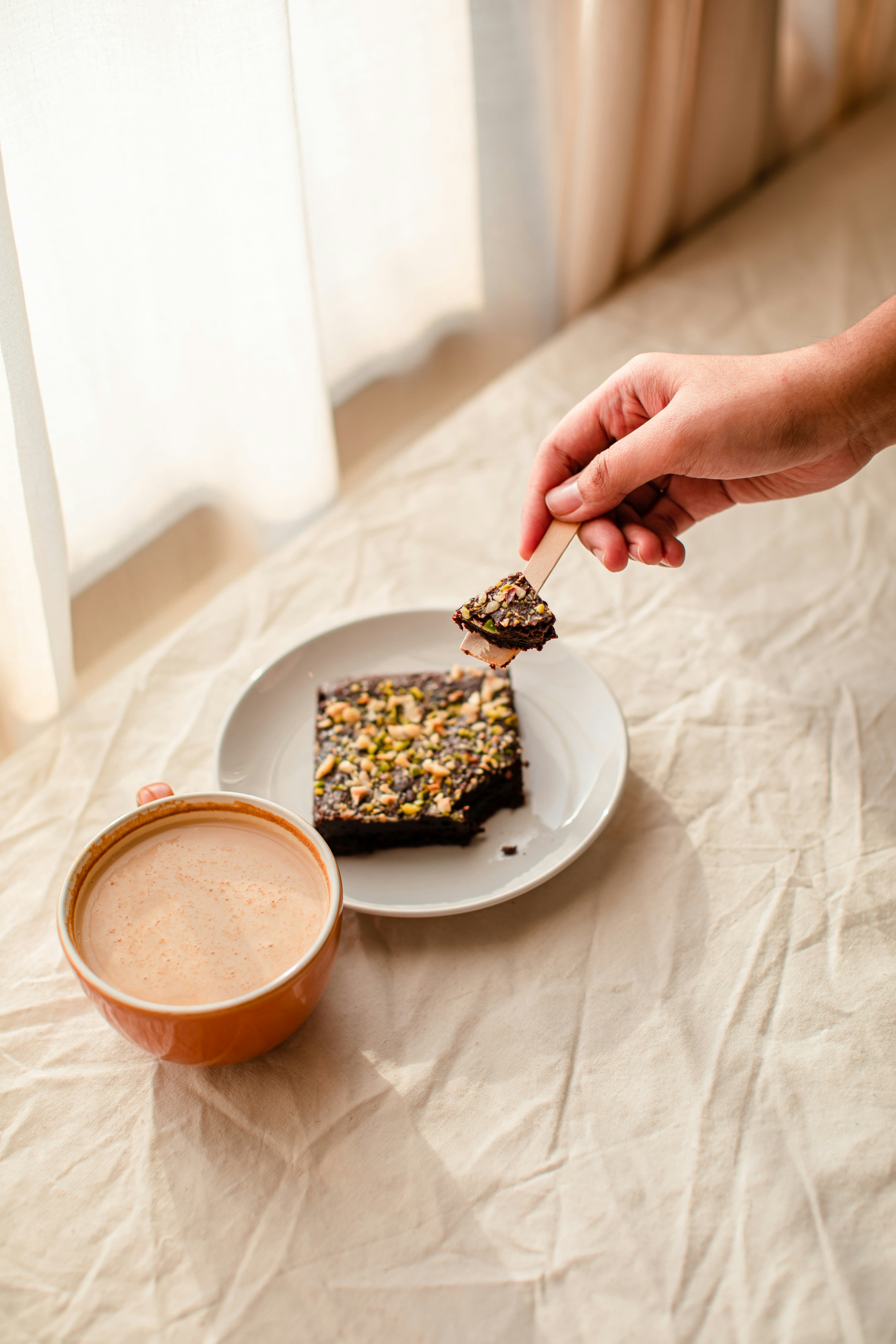 a person holding a spoon over a piece of cake on a plate