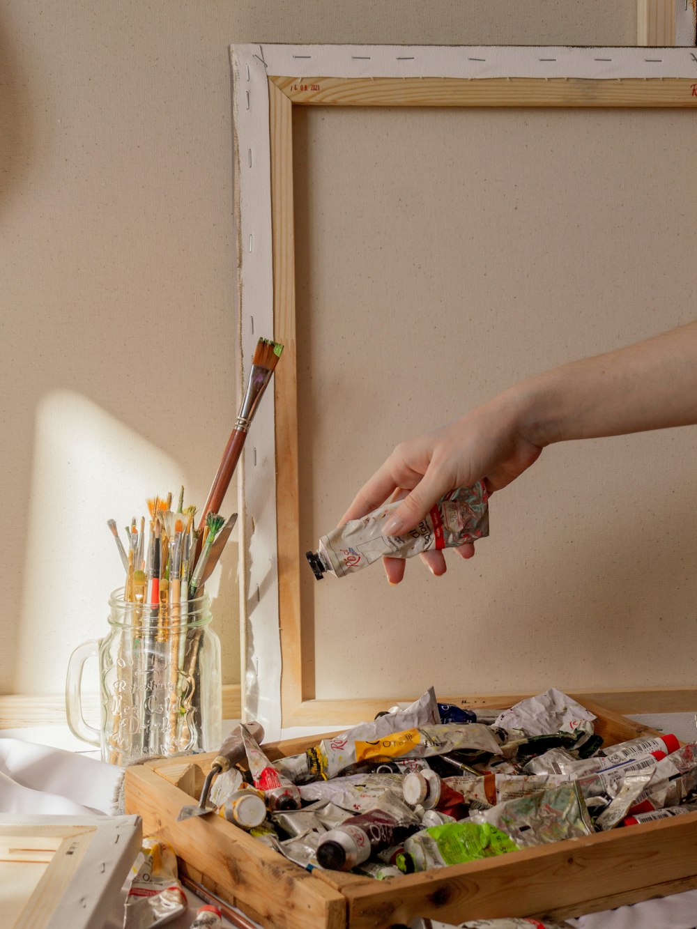 a person reaching for a bottle of paint in a wooden box