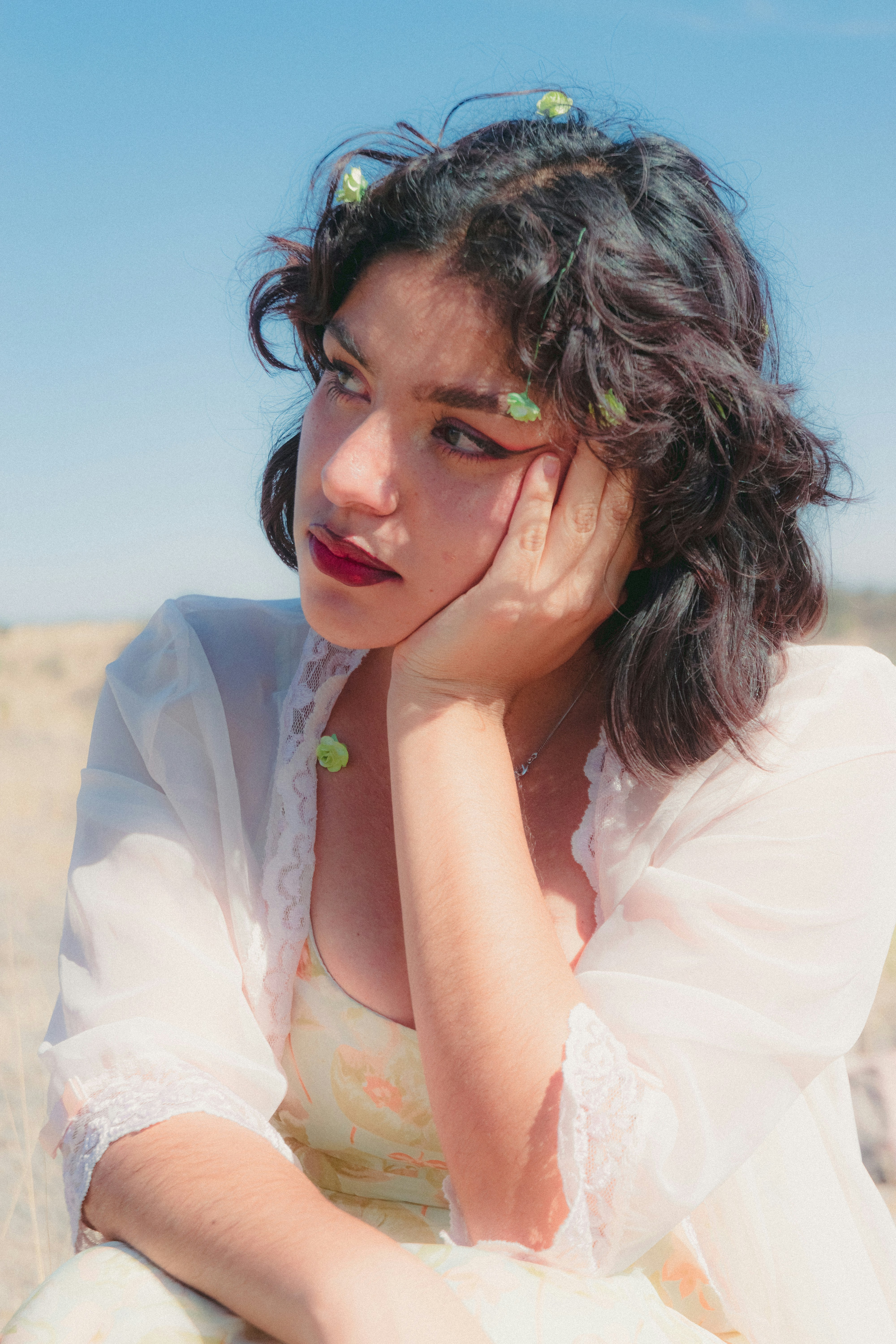 a woman sitting in a field with her hand on her face