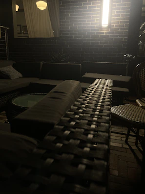 An outdoor seating area with rattan chairs and a metal wall sconce glowing at dusk.