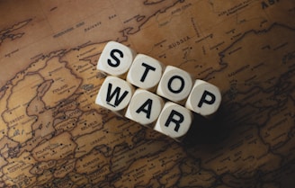 Wooden dice with letters spelling out 'STOP WAR' are placed on a vintage map of Europe and Asia.
