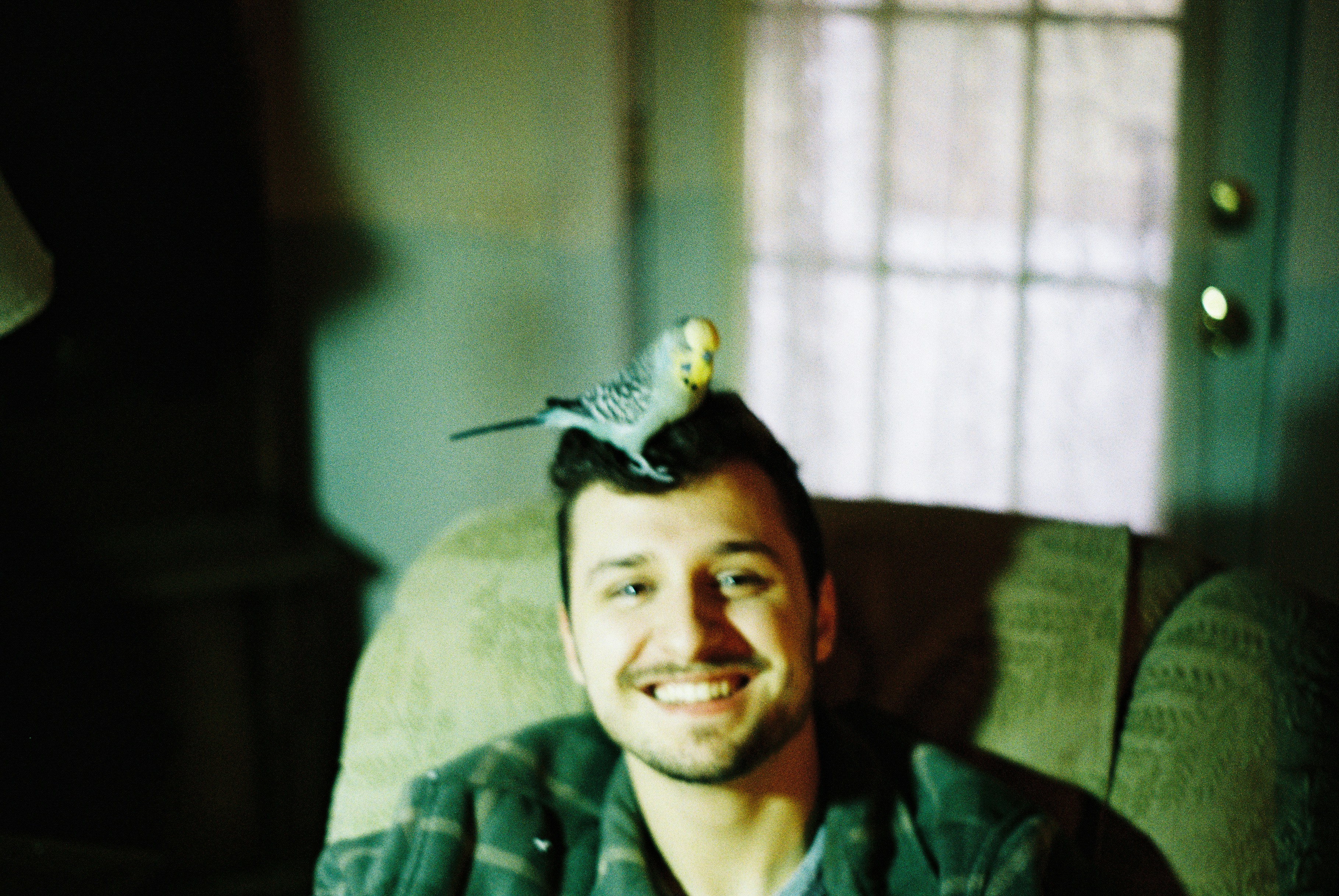 a man sitting in a chair with a bird on top of his head