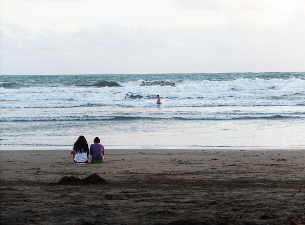 two people sitting on the beach watching the waves