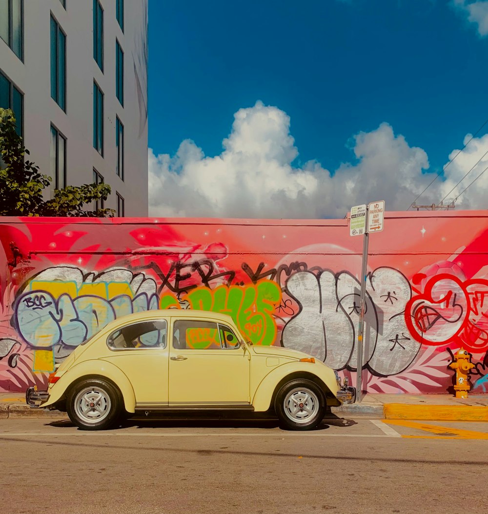 a yellow car parked in front of a graffiti covered wall