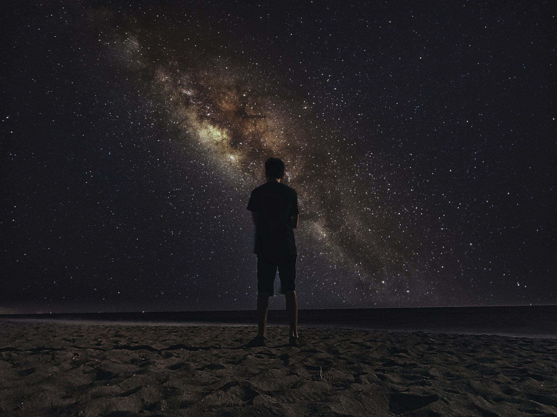 a man standing on top of a sandy beach under a night sky filled with stars