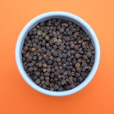 a bowl of black pepper on an orange background