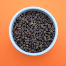 a bowl of black pepper on an orange background