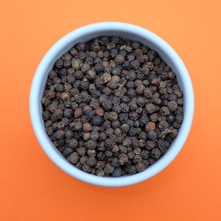 a bowl of black pepper on an orange background