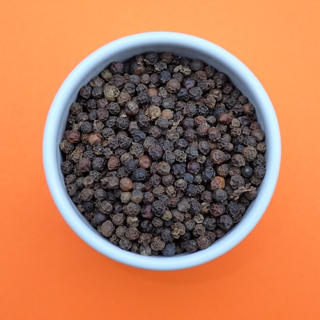 a bowl of black pepper on an orange background