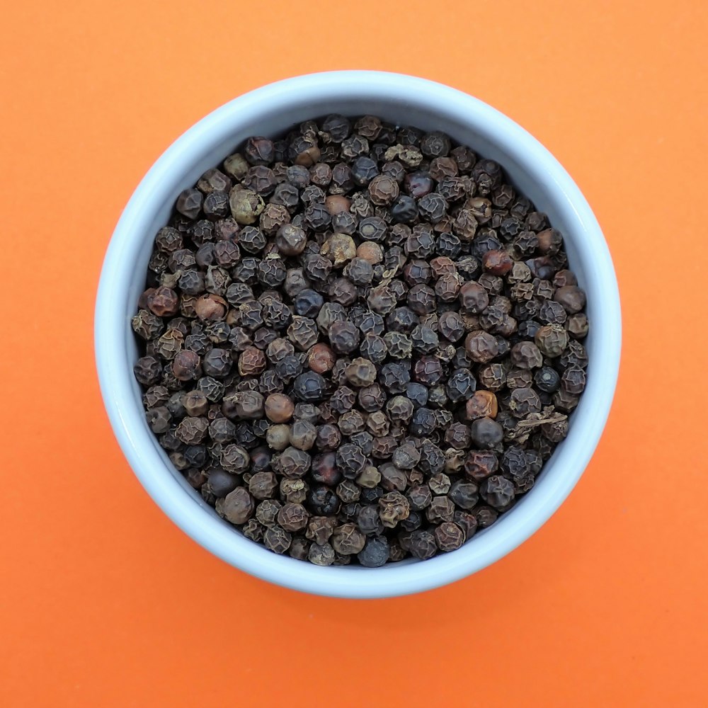 a bowl of black pepper on an orange background