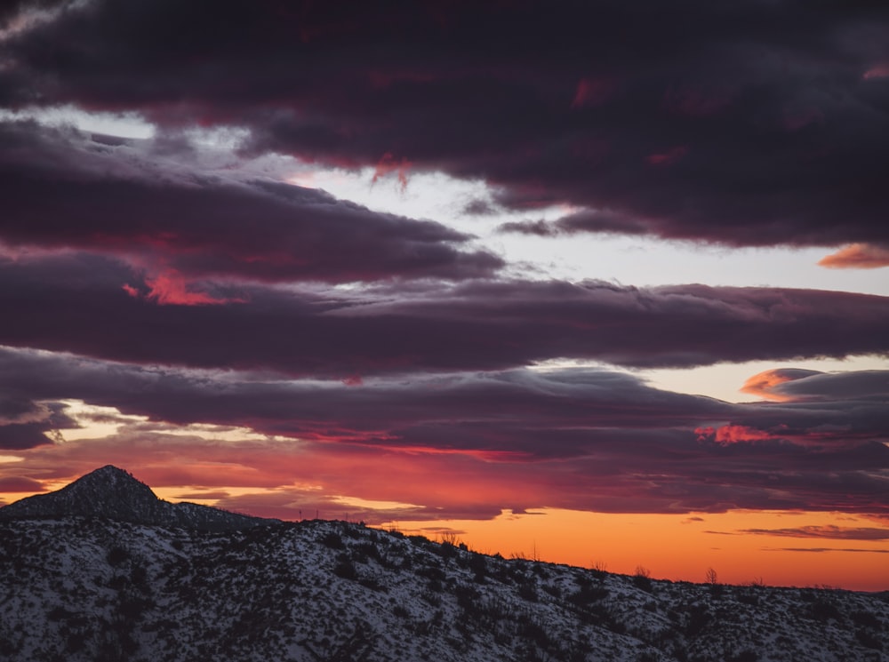 the sun is setting over a mountain with clouds in the sky