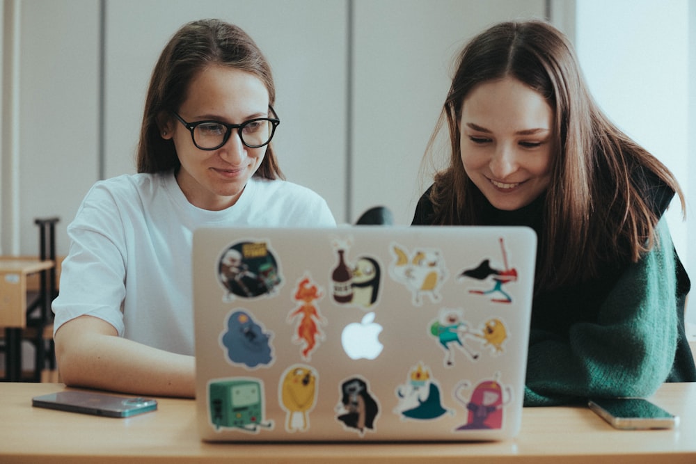 a couple of women sitting at a table with a laptop