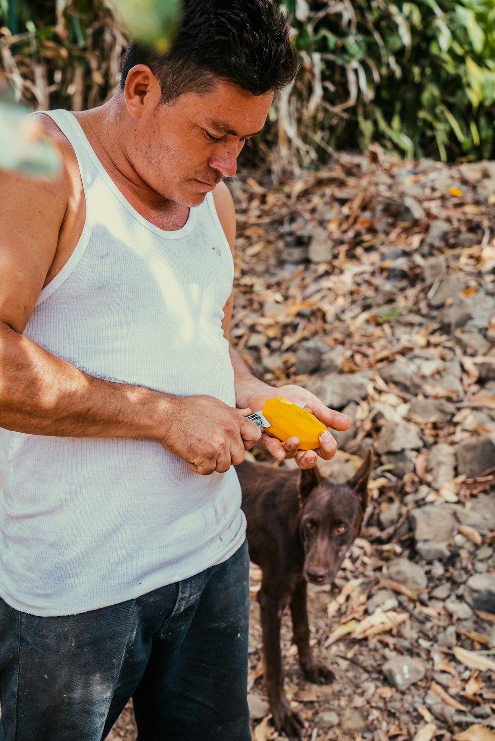 a man in a white tank top holding a banana and a dog