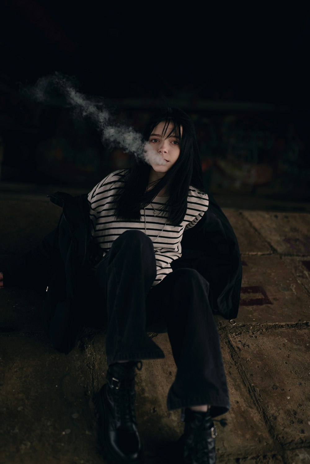 a woman sitting on the ground smoking a cigarette