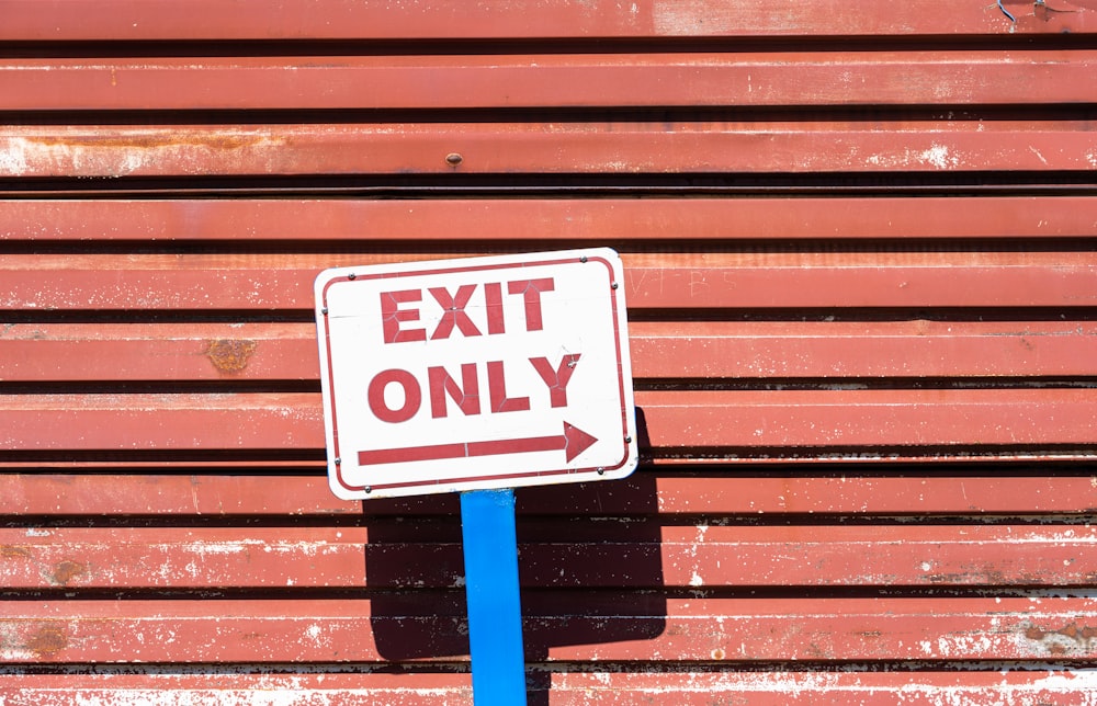 a red and white exit only sign on a blue pole