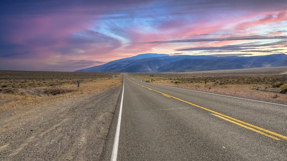 a long empty road with mountains in the background