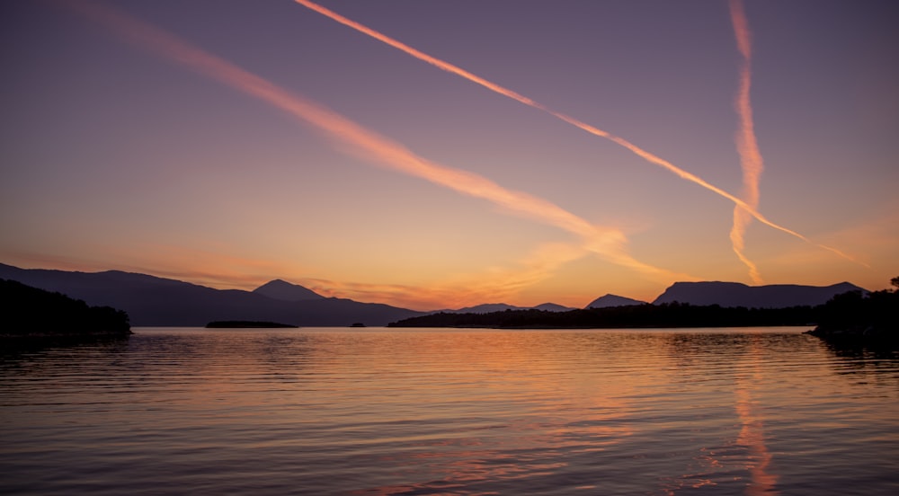 a sunset over a body of water with mountains in the background