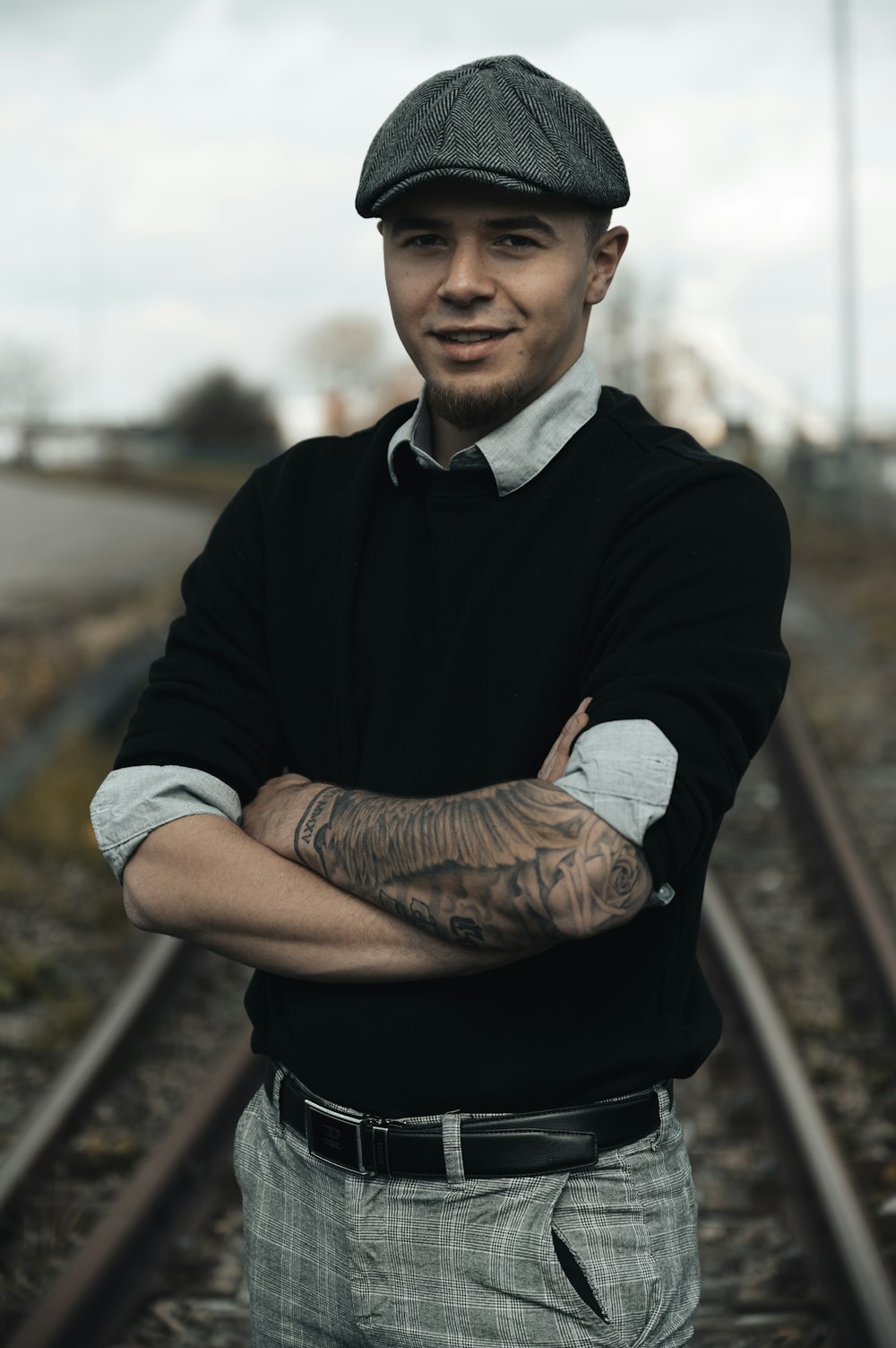 a man with his arms crossed standing in front of a train track