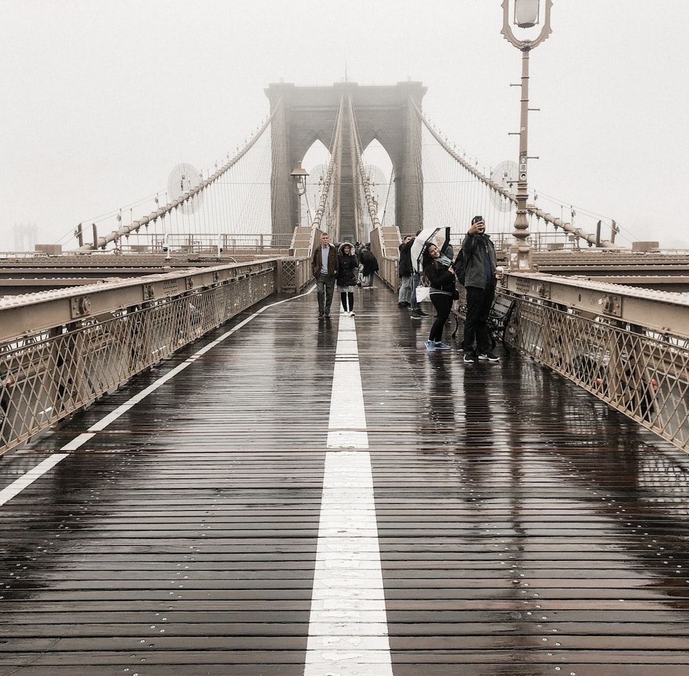 a group of people walking across a bridge in the rain